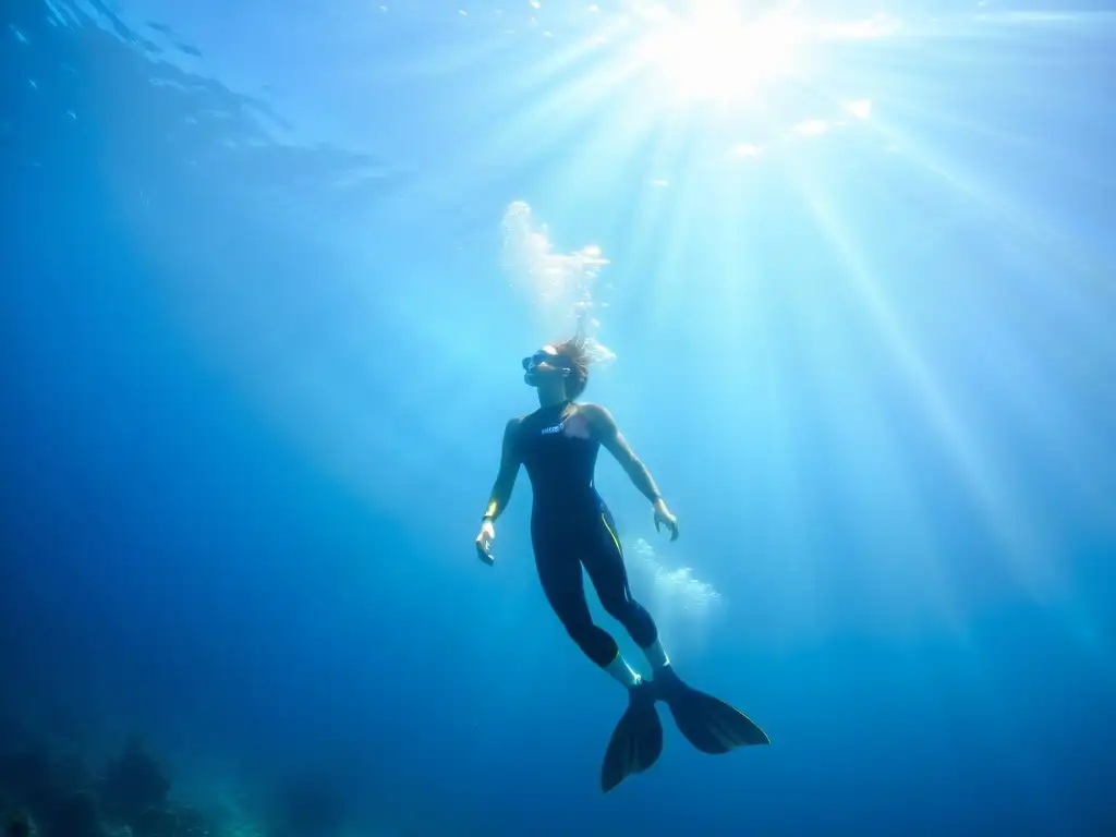 Un buceador libre desciende graciosamente en aguas azules, rodeado de peces tropicales, en un espectáculo de luz y sombra